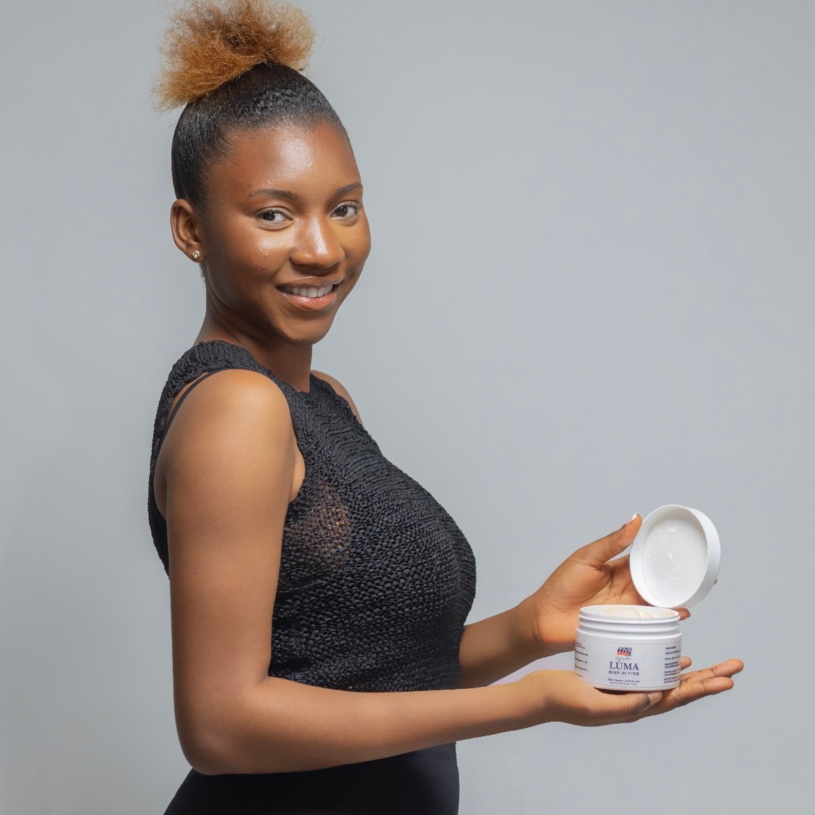 Image of a young model, Holding ip an open container of the Luma body butter